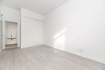 Bedroom in a loft-style house with white built-in wardrobe with sliding doors, light wooden floor...