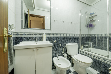 A bathroom with blue and white tiles, a dividing border, a bathtub with a glass screen, a mirror...