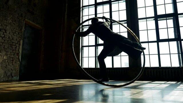 man in black cloak dancing with hoop, performing acrobatic tricks in dancehall, silhouette