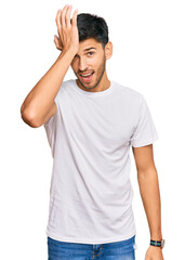 Young handsome man wearing casual white tshirt surprised with hand on head for mistake, remember error. forgot, bad memory concept.