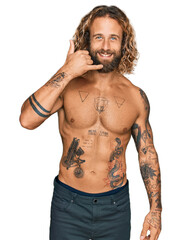 Handsome man with beard and long hair standing shirtless showing tattoos smiling doing phone gesture with hand and fingers like talking on the telephone. communicating concepts.