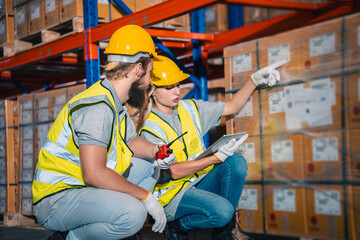 Warehouse worker logistic team wearing hard hat working in aisle between tall racks with packed...