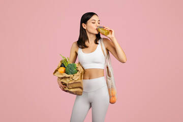 Sporty caucasian woman in sportswear sipping nutritious smoothie and holding bag of fresh...