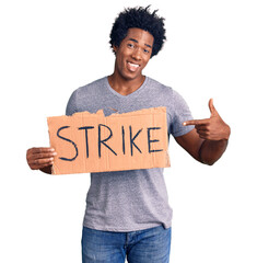 Handsome african american man with afro hair holding strike banner cardboard smiling happy pointing...