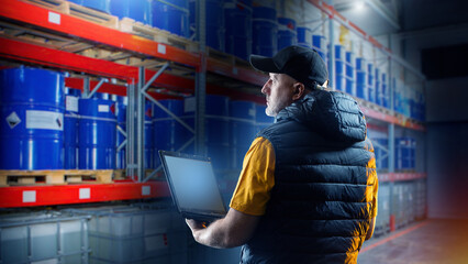 Man in fuel warehouse. Storekeeper with laptop. Warehouse with blue oil barrels. Storage fuel...
