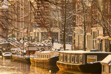 Winter view of Amsterdam with snow and house boats during sunset