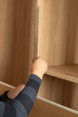 A man measures a wooden board with a ruler. Assembling a wooden product - a cabinet.