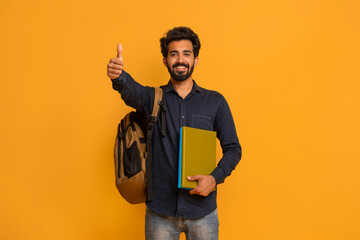 Happy indian student guy with backpack and notebooks showing thumbs up gesture