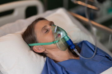 Senior woman in hospital ward, in an oxygen mask, appears to be resting in a deep sleep.