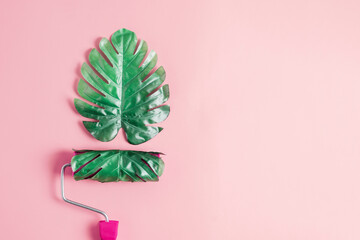 Paint roller with monstera leaf on pink background with copy space. Creative concept for summer.