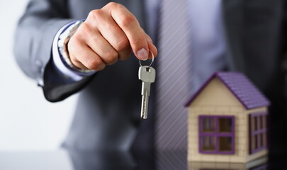 Male hand hold silver key giving it to buyer or take it closeup. New owner pledge idea for life, family solution man arm credit negotiation clerk in office future plan concept