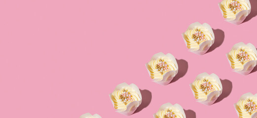 Pattern made from cupcakes with cream and decorating on pink background. Banner with copy space.