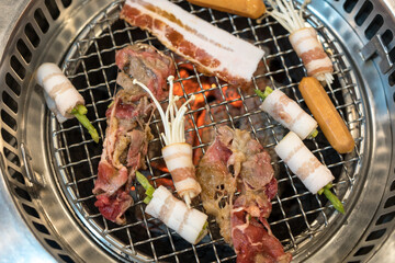 Raw beef and bacon roll with enoki mushroom and vegetable on yakiniku stove which has hot charcoal....