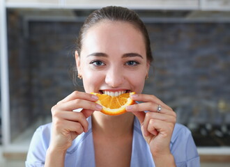 Beautiful brunette smiling woman eat sliced raw tasty orange half at kitchen in the morning portrait. Weight loss beauty fit concept