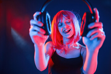 Enjoy the music, holding headphones. Woman with white hair is in studio with neon colors