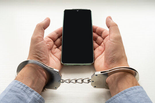 a phone fraudster in handcuffs with a smartphone. Handcuffs man's hands and mobile phone. Concept of addiction.