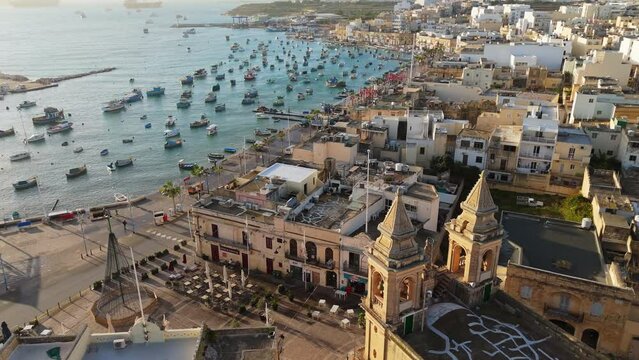 Famous fishing village in Malta - Marsaxlokk. Aerial view of Marsaxlokk with lot of fishing boats in port and church. Morning UHD 4K shot