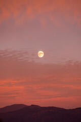 orange moon in the evening sky. full moon during sunset in evening sky. evening dusk orange red and yellow moon. Real photo.