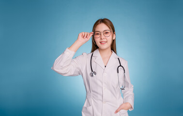 Portrait of smiling female doctor and keeping glasses. Young asian doctor wear medical uniform lab coat and stethoscope isolated over blue color background. Healthcare and medical staff concept.