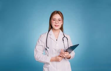 Young asian doctor wear medical uniform lab coat and stethoscope on blue background. Smiling female doctor holding diagnosis in digital tablet and looking at camera.