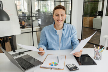 Smiling millennial caucasian guy manager with laptop, colored diagram, tablet with empty screen