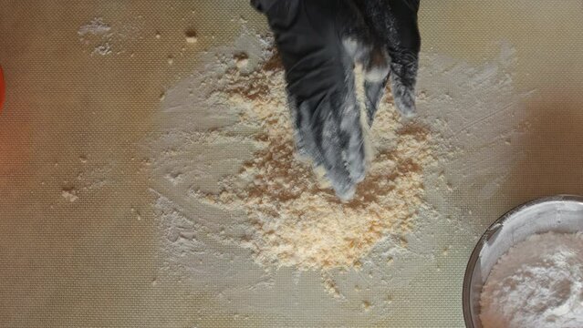Mixing flour with powdered sugar and egg yolks by hand to obtain a shortbread dough. The process of making dough on a silicone mat