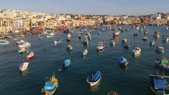 Flying over colorful boats in port of fishing village Marsaxlokk, Malta. Aerial view of Marsaxlokk at sunrise
