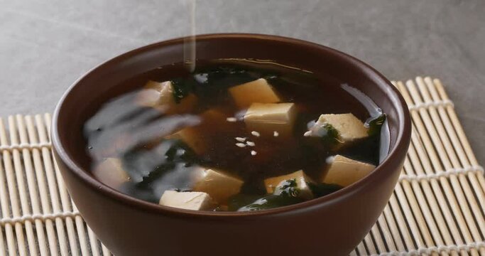 Japanese miso soup in a brown bowl. Close-up footage on the rotating table. Chopsticks take tofu.