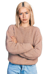 Beautiful young blonde woman wearing brown sweater skeptic and nervous, disapproving expression on face with crossed arms. negative person.