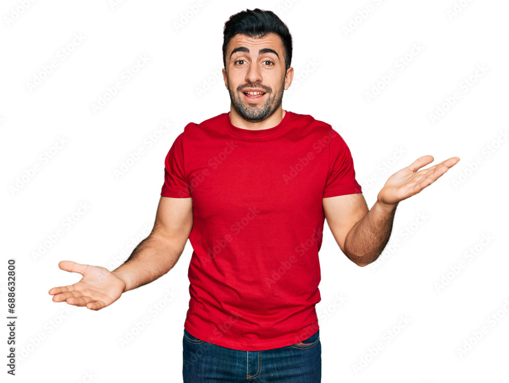 Wall mural Hispanic man with beard wearing casual red t shirt clueless and confused expression with arms and hands raised. doubt concept.