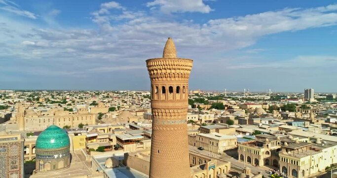 A drone flies around the tower of an ancient complex Kalyan Minaret on a cloudy sunny day. Old Bukhara, Uzbekistan.