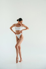 Full height photo. Woman in white underwear with slim body type against white background