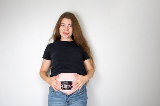 Pregnant Caucasian woman holding ultrasound picture of her baby near baby bump