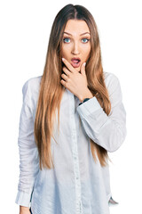 Fototapeta premium Beautiful caucasian woman wearing casual white shirt looking fascinated with disbelief, surprise and amazed expression with hands on chin