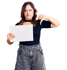 Young beautiful caucasian woman holding blank empty paper with angry face, negative sign showing dislike with thumbs down, rejection concept
