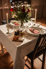 holidays, romantic date and celebration concept - close up of festive table serving for two with flowers in vase and candles burning at home on valentine's day