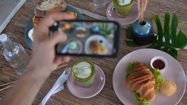 Top view food blogger taking pictures of breakfast in cafe. Womans hands take pictures of food on phone in trendy style for social networks. Breakfast with healthy and delicious food with friends
