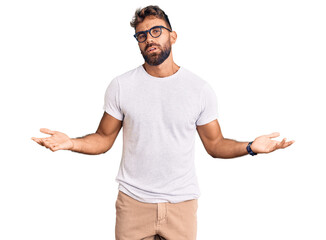 Young hispanic man wearing casual clothes and glasses clueless and confused with open arms, no idea...