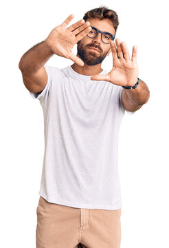 Young hispanic man wearing casual clothes and glasses doing frame using hands palms and fingers, camera perspective