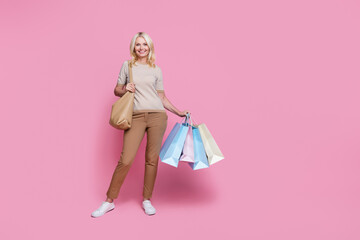 Full length photo of cheerful glad lady dressed striped trendy clothes hold packages empty space isolated on pink color background
