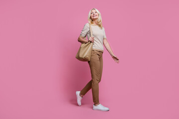 Full length profile photo of lovely positive person hold bag walking look empty space isolated on pink color background