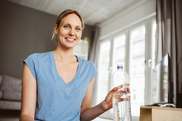 Blonde 30-Year-Old Woman Enjoying Refreshing Water After Workout in Her Cozy Living Room