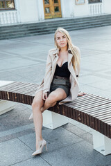 Beautiful blonde woman sitting on a bench on a walk near the building