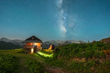 A highland house with lights on stars on the sky and milky way at night