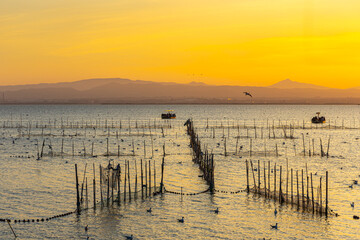Obraz premium A boat with tourists and fishermen on a lake with fish nets and sunny path against the backdrop of an orange sunset
