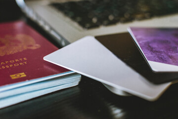 image of some cards next to a passport and an agenda, and next to a laptop on a desk in natural...