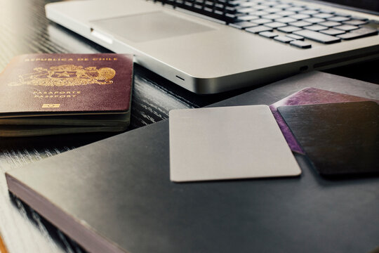 image of some cards next to a passport and an agenda, and next to a laptop on a desk in natural daylight