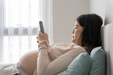 Pregnant asian woman holding smartphone at home using mobile app for pregnant women
