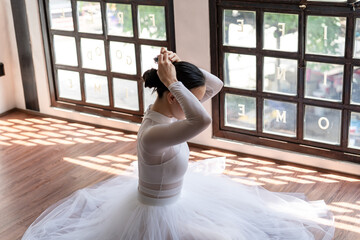 Naklejka premium Asian girl ballet dancer preparing fixing her hair into a bun during ballet class. ballerina adjusting her hair 