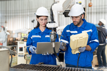 Male and female engineer training using remote controller control robot arm welding machine in...